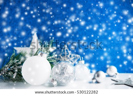 Silver and white christmas ornaments on blue bokeh background with blurred snow. Merry christmas card. Winter holiday snowing xmas theme. Happy New Year