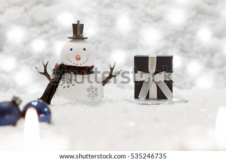 Gift box and snowman are in the snow. Christmas decoration, beautiful bokeh is in the background. 