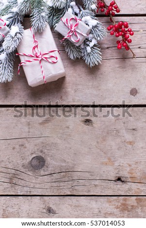 Border from wrapped christmas presents, fur tree branches, red berries on aged wooden background. Selective focus. Place for text.
