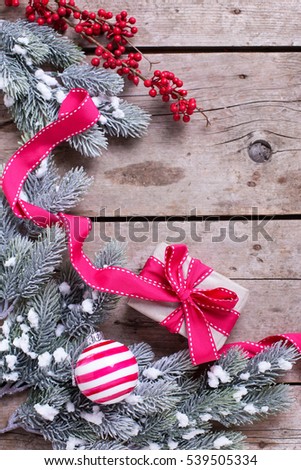 Wrapped christmas gift box, ball, red winter berries and fur tree branches on aged wooden background. Selective focus. Place for text. Vertical image.

