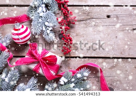 Wrapped christmas gift box, ball, red winter berries and fur tree branches on aged wooden background. Selective focus. Place for text. Drawn snow.