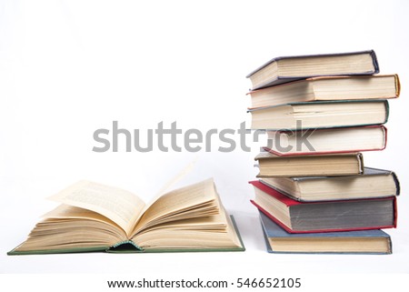 open book in hardcover on a table next to an uneven stack of books with color covers on a white background