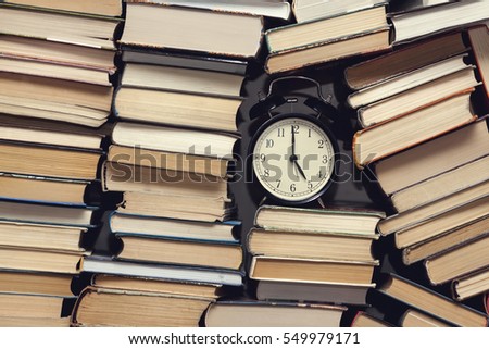alarm clock showing five o'clock among stack of old books background, selective focus, filter applied