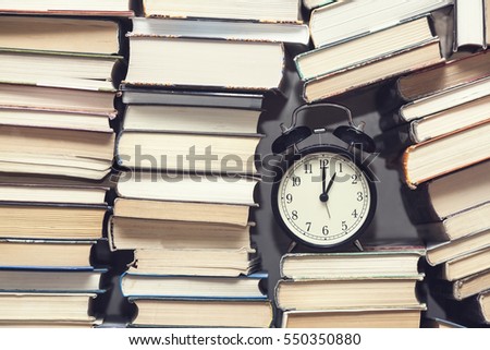 alarm clock showing one o'clock among stack of old books background, selective focus, filter applied
