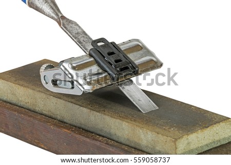 Close up studio shot of chisel clamped in angle guide jig resting on grinding whetstones on white background