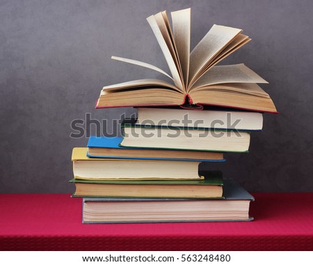 stack of books on the table with a red tablecloth. an open book with curled leaves laying on top.