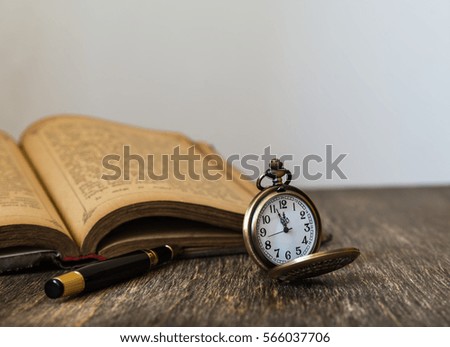 Old book and pocket watch on wooden background.