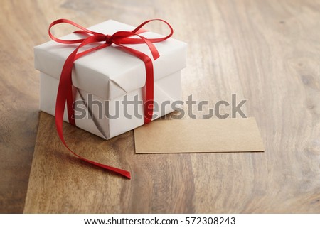 white paper gift box with thin red ribbon and paper card on old wood table, copy space for your text