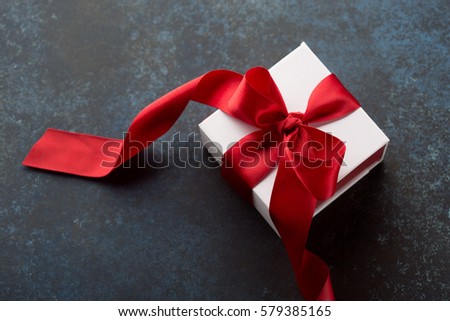 White Gift box with red ribbon on dark blue background. Holiday Birthday Valentines day concept. Selective focus