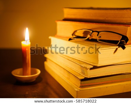 stack of old tattered book on a wooden table lighted candle and glasses