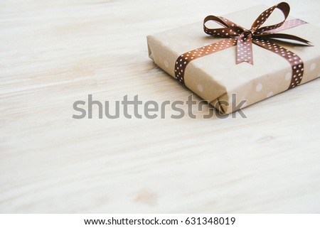 Box in craft paper, eco paper on the wooden table. Top view. Brown paper wrapped gift box with satin ribbon bow on a old rustic blue wood background. For your design. Retro filter. Copy space for text