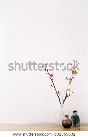 Front view of cotton branches and beauty stylish vase at white background. Minimalistic decorated home office desk.