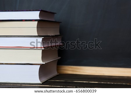 School concept. Stack of books close up on wooden desk with chalkboard as background