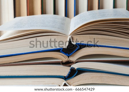 In the foreground a stack of books with an open book on top, in the background the books stand in a row (background)