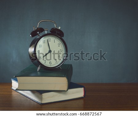 A stack of books and a black alarm clock on the background of a school board