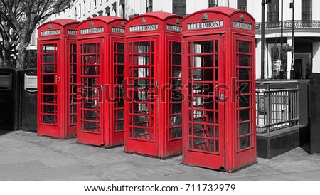Black and white image with four colour color popped red uk telephone boxes in a line in a london street