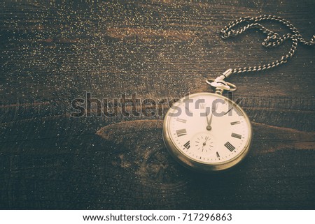 New year clock. Old pocket watch on a wooden background in vintage tones. New Year's background with hours over time 23:55.