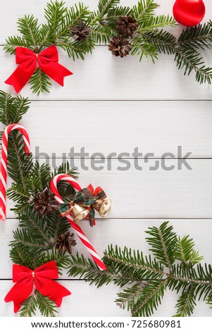Sweet christmas background. Traditional candy canes, fir tree branches and red bows border on white wood. Xmas and other winter holidays concept with copy space, top view, vertical