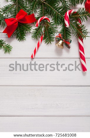 Sweet christmas background. Traditional candy canes, fir tree branches and red bow border on white wood. Xmas and other winter holidays concept with copy space, top view, vertical