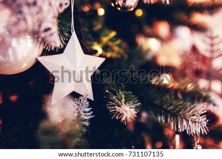 Paper star on a fir-tree as a christmas close up and beautiful holiday background with a lot of other toys and garlands on a branches