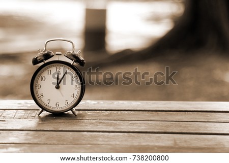 Retro Alarm Clock on wooden table texture over blur background. Sephia tone