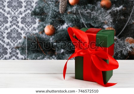 Christmas present decorated with red ribbon on table, closeup, selective focus. Christmas tree background.