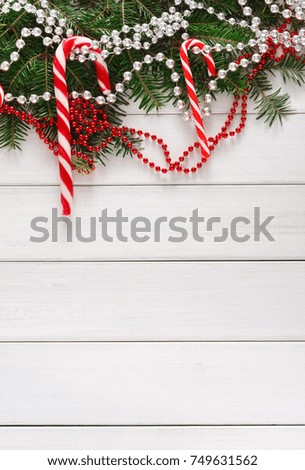 Christmas background. Traditional candy canes, fir tree branches and beads garland border on white wood. Xmas and other winter holidays concept with copy space, top view, vertical
