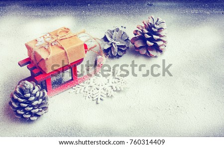 Christmas card with red sled, gift box, pine cones, black background covered snow, space for text, closeup, toned