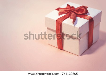 white  gift box with thin red ribbon on pink background