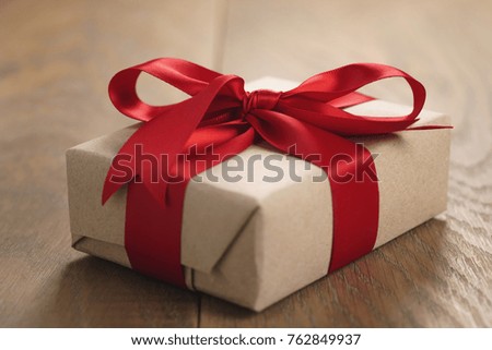 brown paper gift box with red ribbon bow on oak table