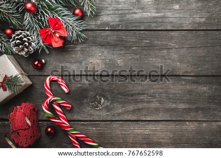 Christmas greeting card on wood background, fir branches, cone, message space, toys, colorful candies and xmas gifts. Top view.