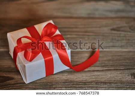 White handmade gift box with shiny red satin ribbon  on dark wooden rustic background. Presents with ribbon for christmas, valentine, birthday or new year for any holiday concept. 