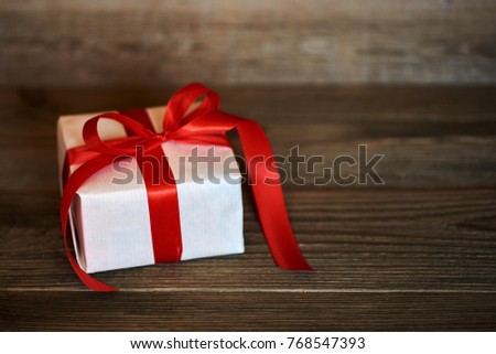 White handmade gift box with shiny red satin ribbon  on dark wooden rustic background. Presents with ribbon for christmas, valentine, birthday or new year for any holiday concept. 