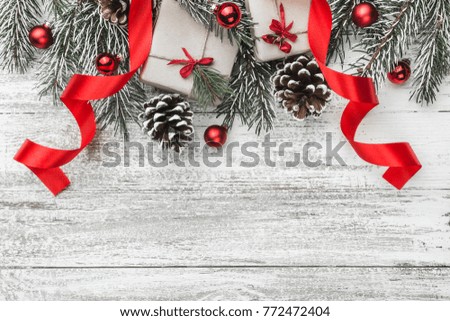 View from above, top, on a white wooden board background with evergreen, fir branch with pines, gift, present boxes, ribbon and red tree globes with space for text, greeting card