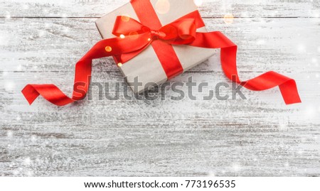 Christmas theme with  present box tied with red ribbon white wooden background viewed from above, in snow, greeting card with space for text