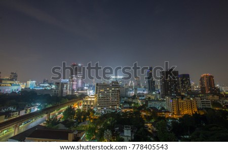 Outdoor panoramic scenic view of the downtown of Bangkok, Thailand at night . Numerous skyscrapers with many bright lights fills with dark greenish gardening trees , sky railway and local street