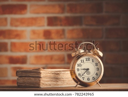 vintage alarm clock and old books on wooden table at brick wall background. Library