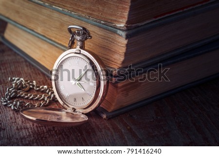 dial Vintage pocket watch on a chain and old books on a wooden background. Tinted picture in low key
