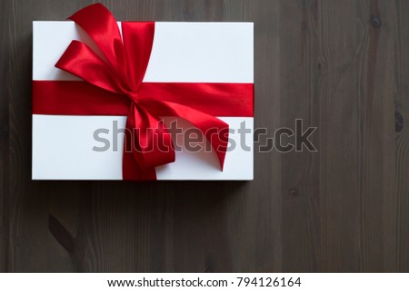 A white gift box decorated with a red satin bow on the table. Space for text