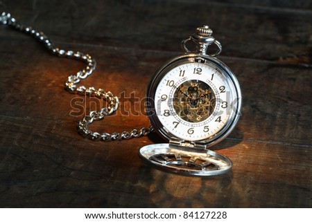 Vintage pocket watch with open lid and chain on wooden surface
